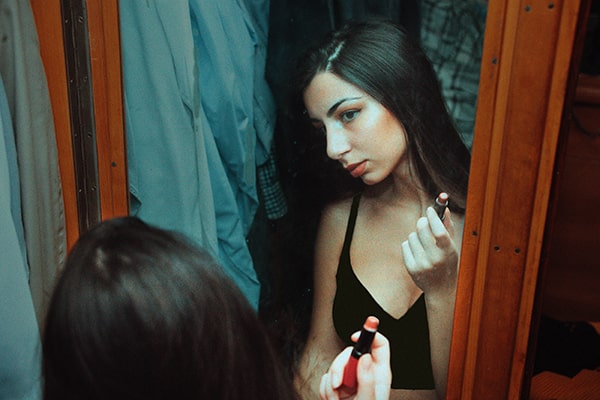 Jovem adolescente se olhando no espelho após passar batom