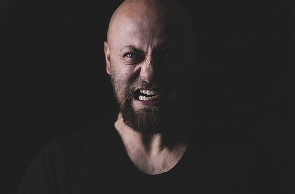 Homem careca com feição de irado, com fundo negro de background