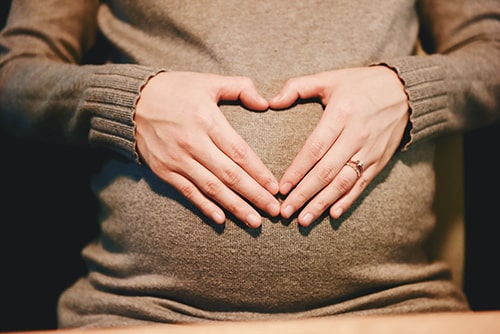 Mulher grávida fazendo símbolo do amor com suas mãos
