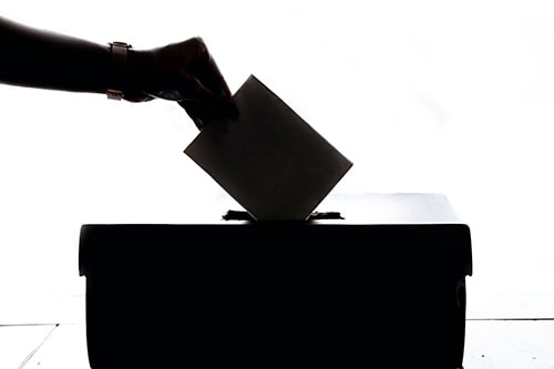 Homem colocando um voto impresso em uma urna