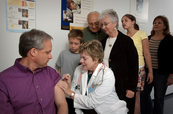 Homem sendo vacinado por enfermeira cm toda sua família assistindo