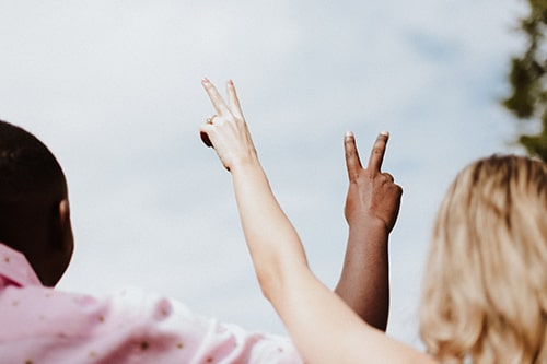 Homem e mulher acenando o símbolo de paz com as mãos;